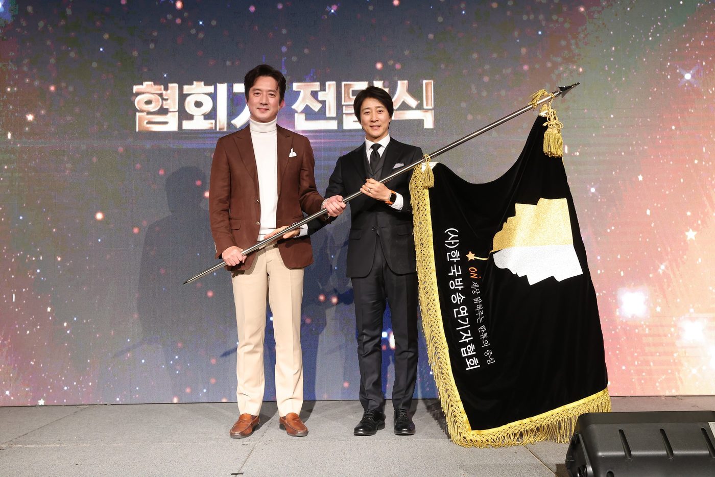 만남day 행사 무대의 협회기 전달식 — 협회기를 함께 든 두 사람