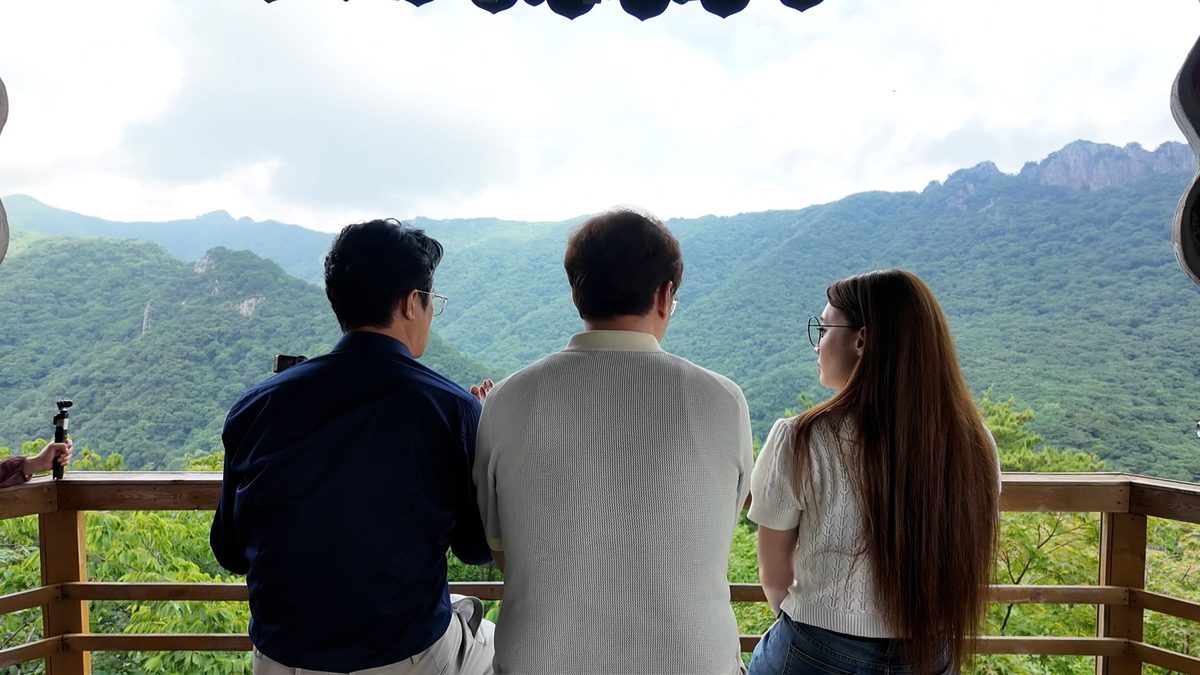 전망대 난간에서 산 풍경을 바라보는 세 사람의 뒷모습