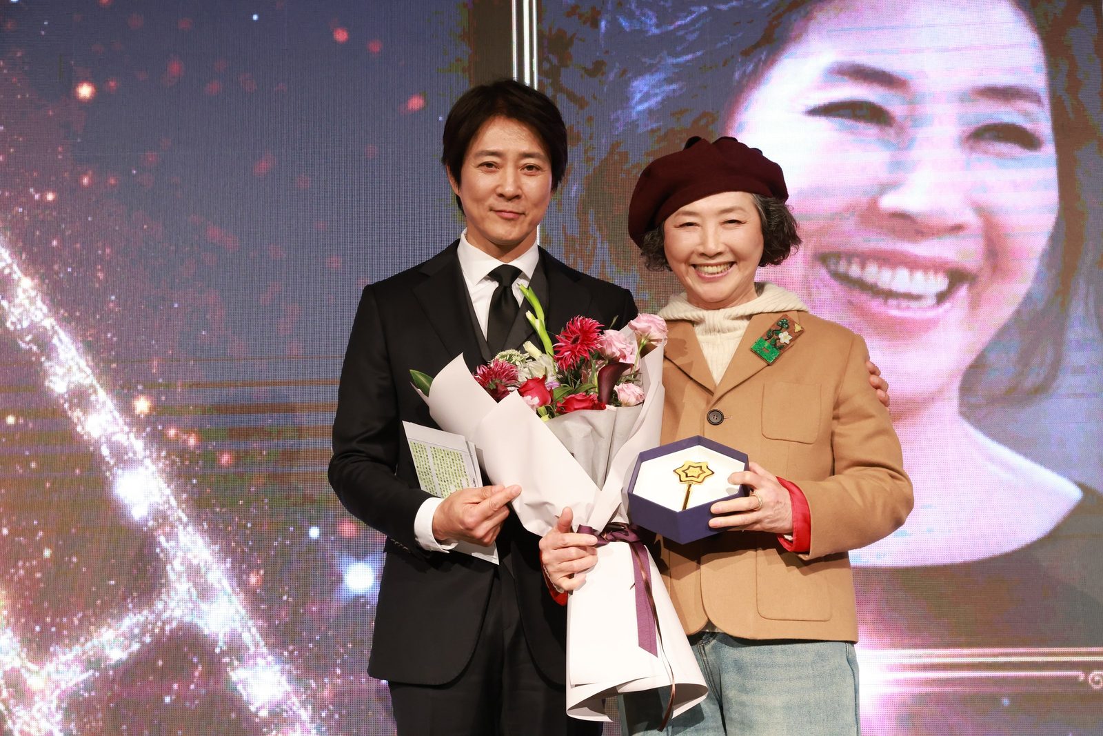 만남day 행사 무대에서 꽃다발과 기념패를 든 두 사람(2024.12.27 롯데호텔 크리스탈볼룸)
